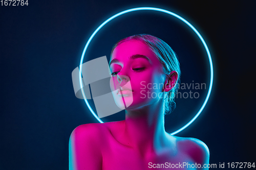Image of Portrait of female fashion model in neon light on dark studio background. Beautiful caucasian woman with trendy make-up, neoned blue circle