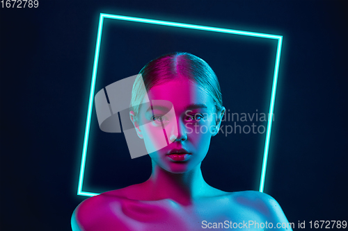 Image of Portrait of female fashion model in neon light on dark studio background. Beautiful caucasian woman with trendy make-up, neoned blue square