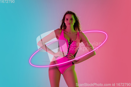 Image of Fashion portrait of young fit and sportive caucasian woman in stylish swimwear on gradient background with pink neoned circle