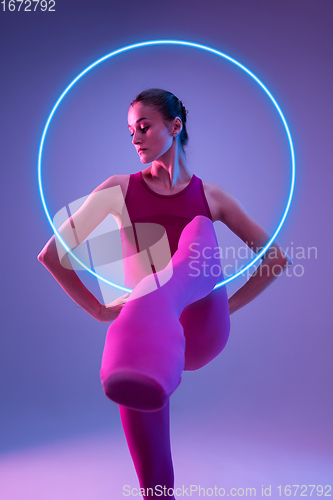 Image of Young and graceful ballet dancer isolated on purple studio background in neon light with glowing neoned circle. Art, motion, action, flexibility, inspiration concept.