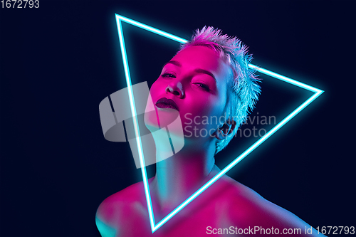 Image of Portrait of female fashion model in neon light on dark studio background. Beautiful caucasian woman with trendy make-up, neoned blue triangle