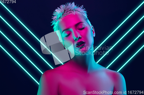 Image of Portrait of female fashion model in neon light on dark studio background. Beautiful caucasian woman with trendy make-up, neoned blue lines