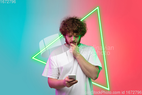 Image of Caucasian man\'s portrait isolated on gradient blue-red studio background in neon light with glowing triangle. Concept of human emotions, facial expression, sales, ad.