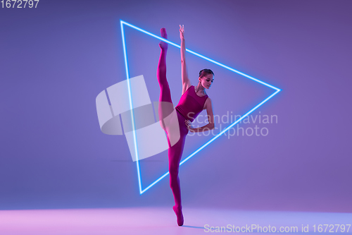 Image of Young and graceful ballet dancer isolated on purple studio background in neon light with glowing neoned triangle. Art, motion, action, flexibility, inspiration concept.