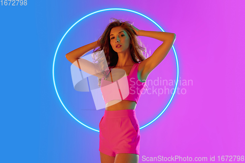 Image of Beautiful seductive girl in fashionable, romantic outfit on gradient background in neon light with glowing neoned blue circle