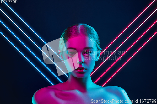 Image of Portrait of female fashion model in neon light on dark studio background. Beautiful caucasian woman with trendy make-up, neoned blue and pink lines