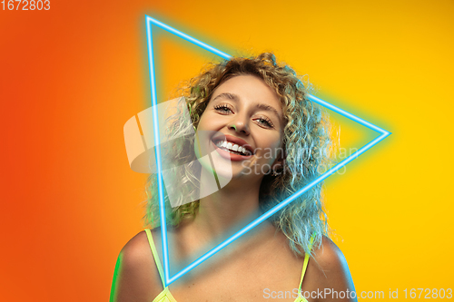 Image of Caucasian woman\'s portrait isolated on gradient studio background in neon light with glowing triangle. Concept of human emotions, facial expression, sales, ad.