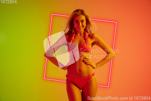 Image of Fashion portrait of young fit and sportive caucasian woman in stylish swimwear on gradient background with pink neoned square