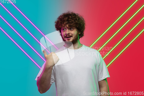 Image of Caucasian man\'s portrait isolated on gradient blue-red studio background in neon light with glowing lines. Concept of human emotions, facial expression, sales, ad.