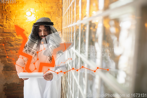 Image of Arabian businessman working in office, business centre using device, gadget. Modern saudi lifestyle. Ethnicity, finance, income increase