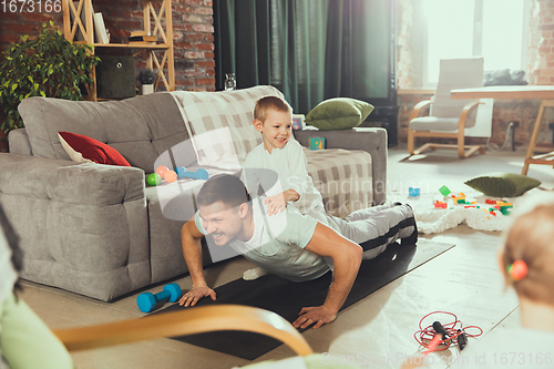 Image of Young man exercising fitness, aerobic, yoga at home, sporty lifestyle. Getting active while his child playing on the background, home gym.