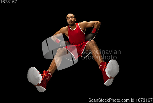 Image of Young african-american boxer in action, motion isolated on black background, look from the bottom. Concept of sport, movement, energy and dynamic.