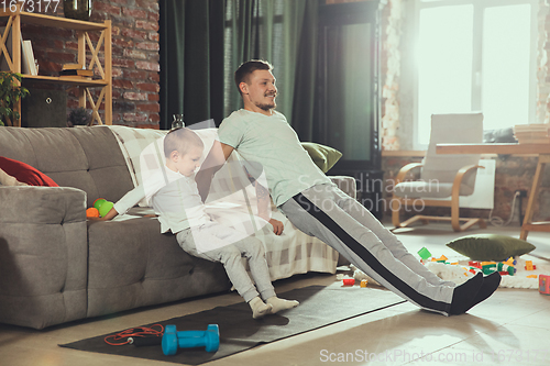 Image of Young man exercising fitness, aerobic, yoga at home, sporty lifestyle. Getting active while his child playing on the background, home gym.