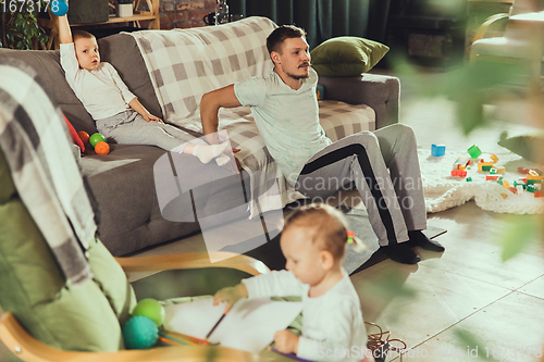 Image of Young man exercising fitness, aerobic, yoga at home, sporty lifestyle. Getting active while his child playing on the background, home gym.