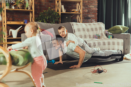 Image of Young man exercising fitness, aerobic, yoga at home, sporty lifestyle. Getting active while his child playing on the background, home gym.