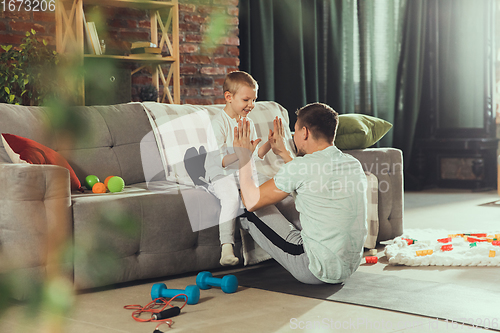 Image of Young man exercising fitness, aerobic, yoga at home, sporty lifestyle. Getting active while his child playing on the background, home gym.