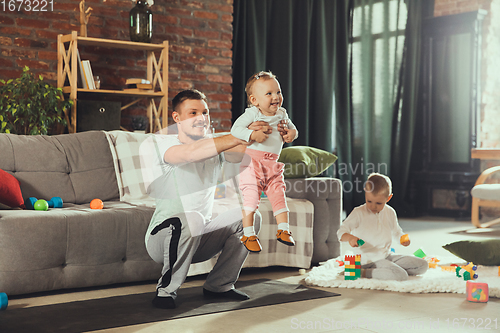 Image of Young man exercising fitness, aerobic, yoga at home, sporty lifestyle. Getting active while his child playing on the background, home gym.