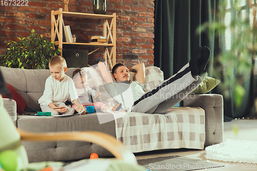 Image of Young man exercising fitness, aerobic, yoga at home, sporty lifestyle. Getting active while his child playing on the background, home gym.