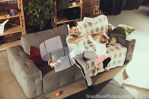 Image of Young man exercising fitness, aerobic, yoga at home, sporty lifestyle. Getting active while his child playing on the background, home gym.