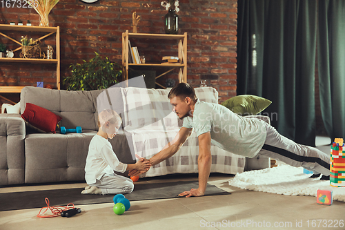 Image of Young man exercising fitness, aerobic, yoga at home, sporty lifestyle. Getting active while his child playing on the background, home gym.