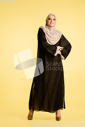 Image of Beautiful arab woman posing in stylish hijab isolated on yellow studio background. Fashion, beauty, style concept