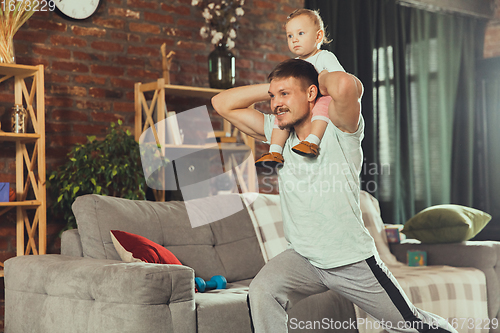 Image of Young man exercising fitness, aerobic, yoga at home, sporty lifestyle. Getting active while his child playing on the background, home gym.