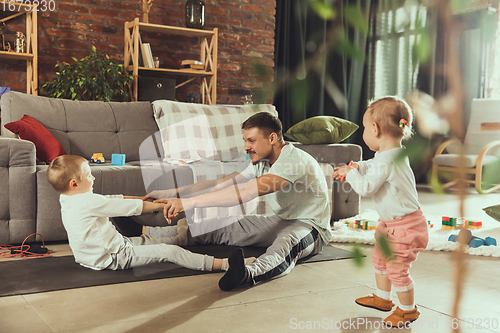 Image of Young man exercising fitness, aerobic, yoga at home, sporty lifestyle. Getting active while his child playing on the background, home gym.