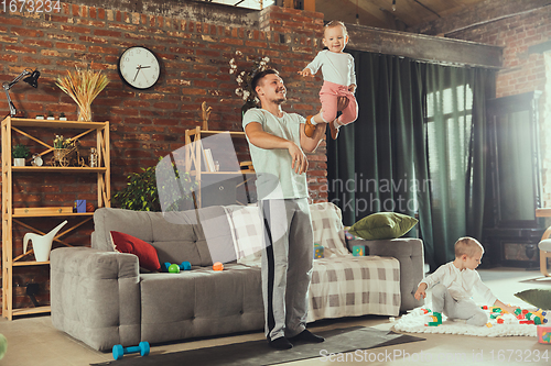 Image of Young man exercising fitness, aerobic, yoga at home, sporty lifestyle. Getting active while his child playing on the background, home gym.