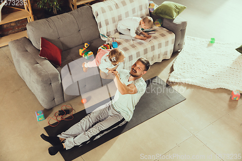 Image of Young man exercising fitness, aerobic, yoga at home, sporty lifestyle. Getting active while his child playing on the background, home gym.