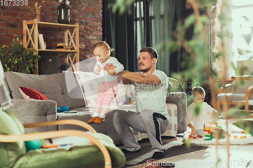 Image of Young man exercising fitness, aerobic, yoga at home, sporty lifestyle. Getting active while his child playing on the background, home gym.