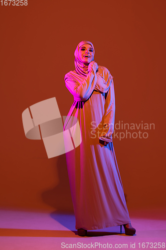 Image of Beautiful arab woman posing in stylish hijab isolated on brown studio background in neon light. Fashion, beauty, style concept