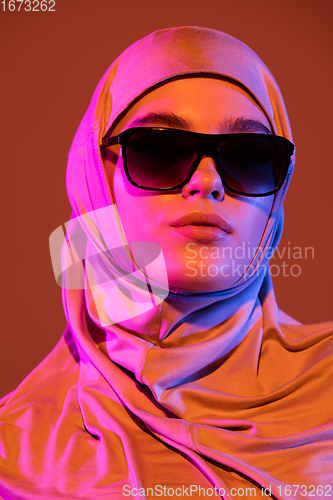 Image of Beautiful arab woman posing in stylish hijab isolated on brown studio background in neon light. Fashion, beauty, style concept