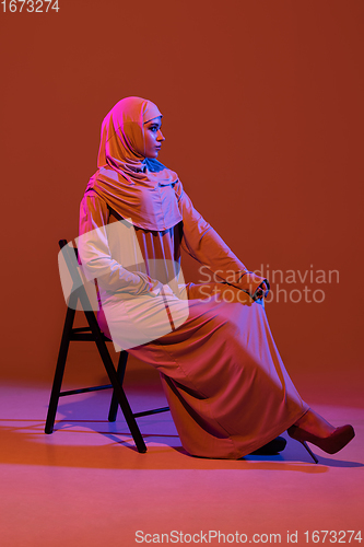 Image of Beautiful arab woman posing in stylish hijab isolated on brown studio background in neon light. Fashion, beauty, style concept