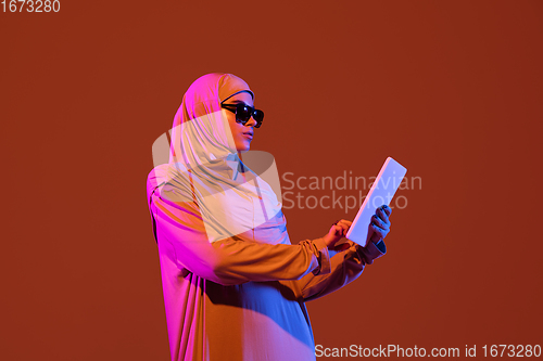 Image of Beautiful arab woman posing in stylish hijab isolated on brown studio background in neon light. Fashion, beauty, style concept