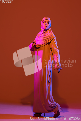 Image of Beautiful arab woman posing in stylish hijab isolated on brown studio background in neon light. Fashion, beauty, style concept