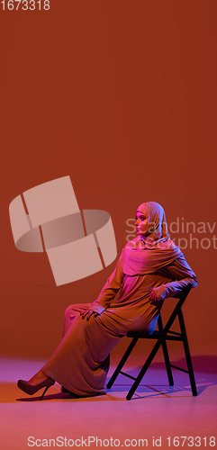 Image of Beautiful arab woman posing in stylish hijab isolated on brown studio background in neon light. Fashion, beauty, style concept