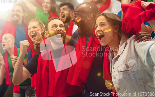 Image of German football, soccer fans cheering their team with a red scarfs at stadium. Excited fans cheering a goal, supporting favourite players