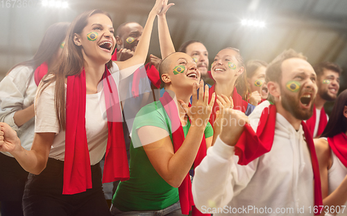 Image of Brazilian football, soccer fans cheering their team with a red scarfs at stadium. Excited fans cheering a goal, supporting favourite players