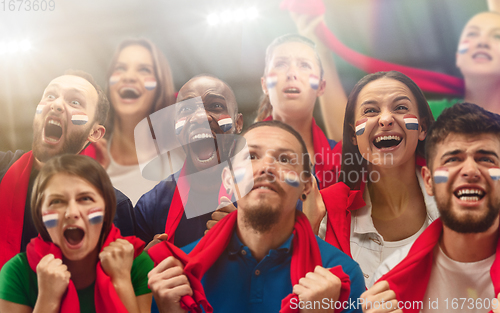 Image of Netherlands football, soccer fans cheering their team with a red scarfs at stadium. Excited fans cheering a goal, supporting favourite players