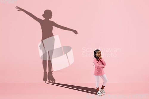 Image of Childhood and dream about big and famous future. Conceptual image with girl and shadow of fit female figure skater on coral pink background