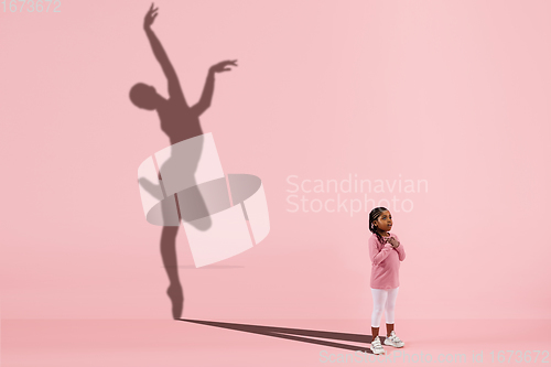 Image of Childhood and dream about big and famous future. Conceptual image with girl and shadow of fit female ballet dancer on coral pink background