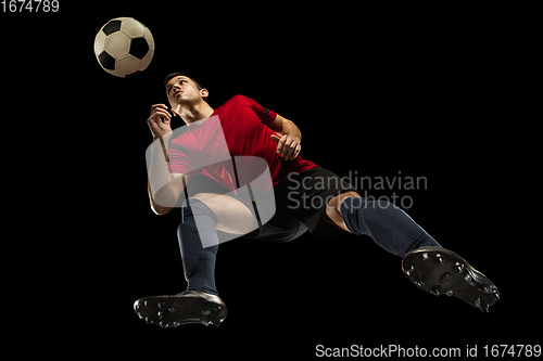 Image of Young caucasian football, soccer player in action, motion isolated on black background, look from the bottom. Concept of sport, movement, energy and dynamic.