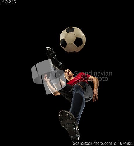 Image of Young caucasian football, soccer player in action, motion isolated on black background, look from the bottom. Concept of sport, movement, energy and dynamic.