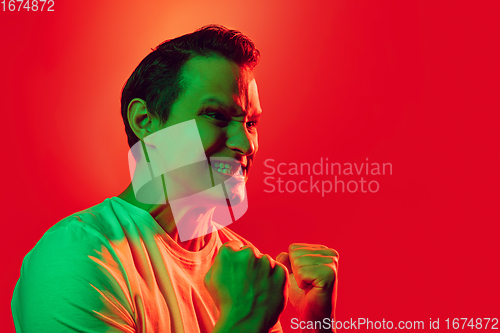 Image of Caucasian man\'s portrait isolated on red studio background in multicolored neon light