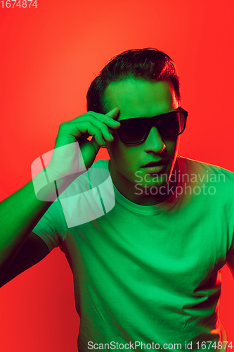 Image of Caucasian man\'s portrait isolated on red studio background in multicolored neon light