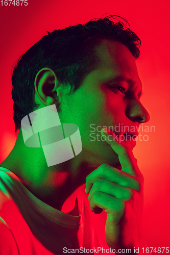 Image of Caucasian man\'s portrait isolated on red studio background in multicolored neon light