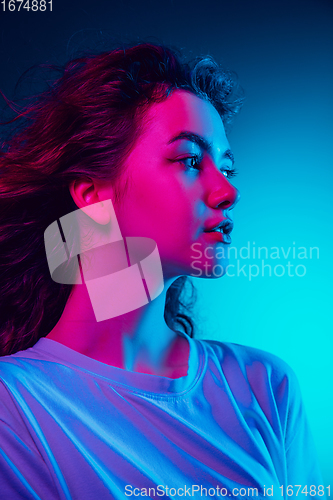 Image of Caucasian woman\'s portrait isolated on blue studio background in multicolored neon light