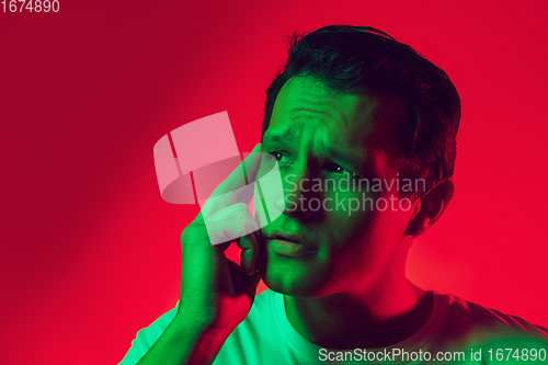 Image of Caucasian man\'s portrait isolated on red studio background in multicolored neon light