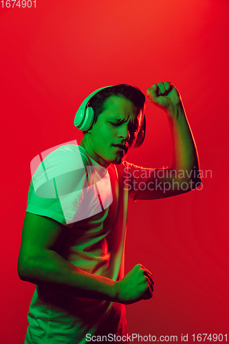 Image of Caucasian man\'s portrait isolated on red studio background in multicolored neon light