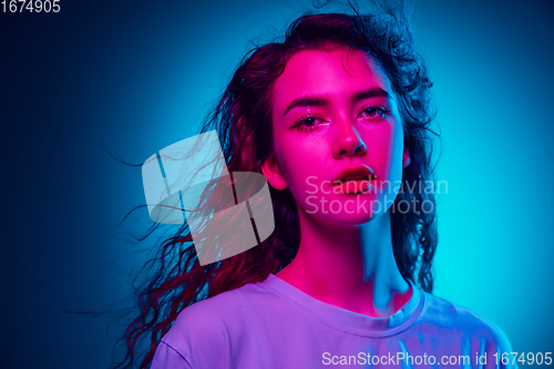 Image of Caucasian woman\'s portrait isolated on blue studio background in multicolored neon light